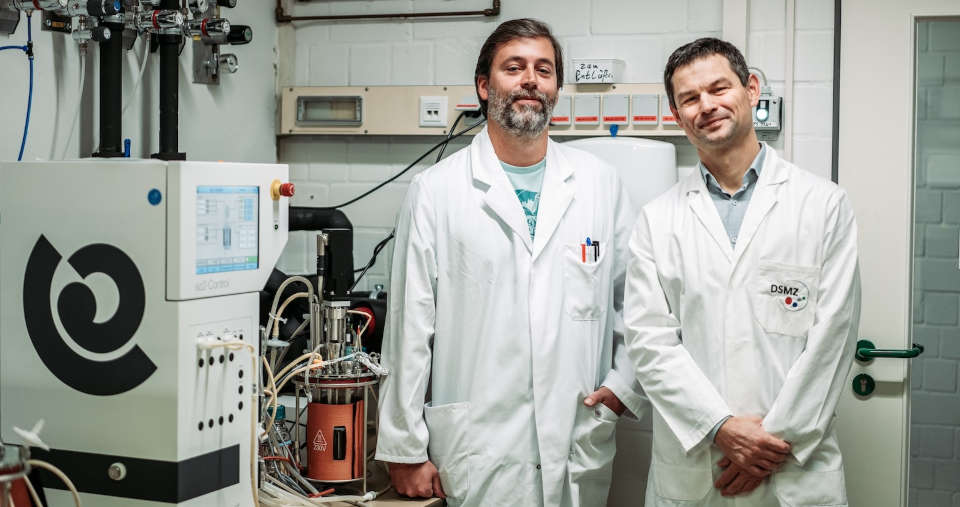 Dr. Stefan Dyskma (li.) und Prof. Dr. Michael Pester neben einem Bioreaktor bei der DSMZ, in dem neuartige „Sulfatreduzierer“ untersucht werden konnten. Foto: DSMZ Wissenschaftler stellen sich in einem Labor dem Fotografen